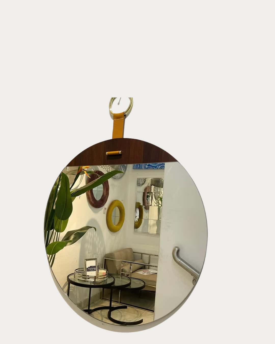 Leather Wooden Frameless mirror with a leather strap hanging on a wall, reflecting a cozy seating ar.