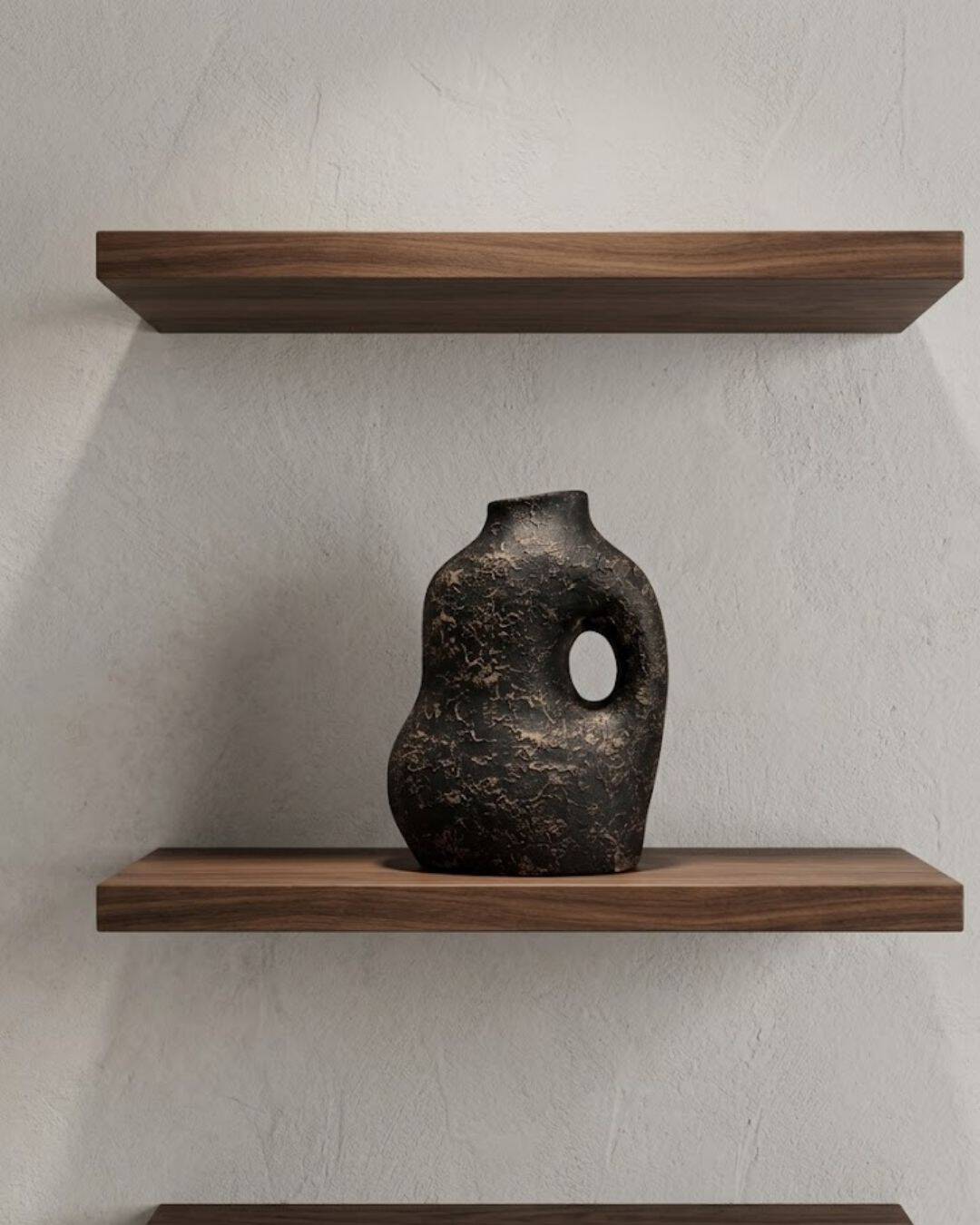 Cream and bronze textured irregular shape vase with a circular handle, displayed on wooden shelves i.