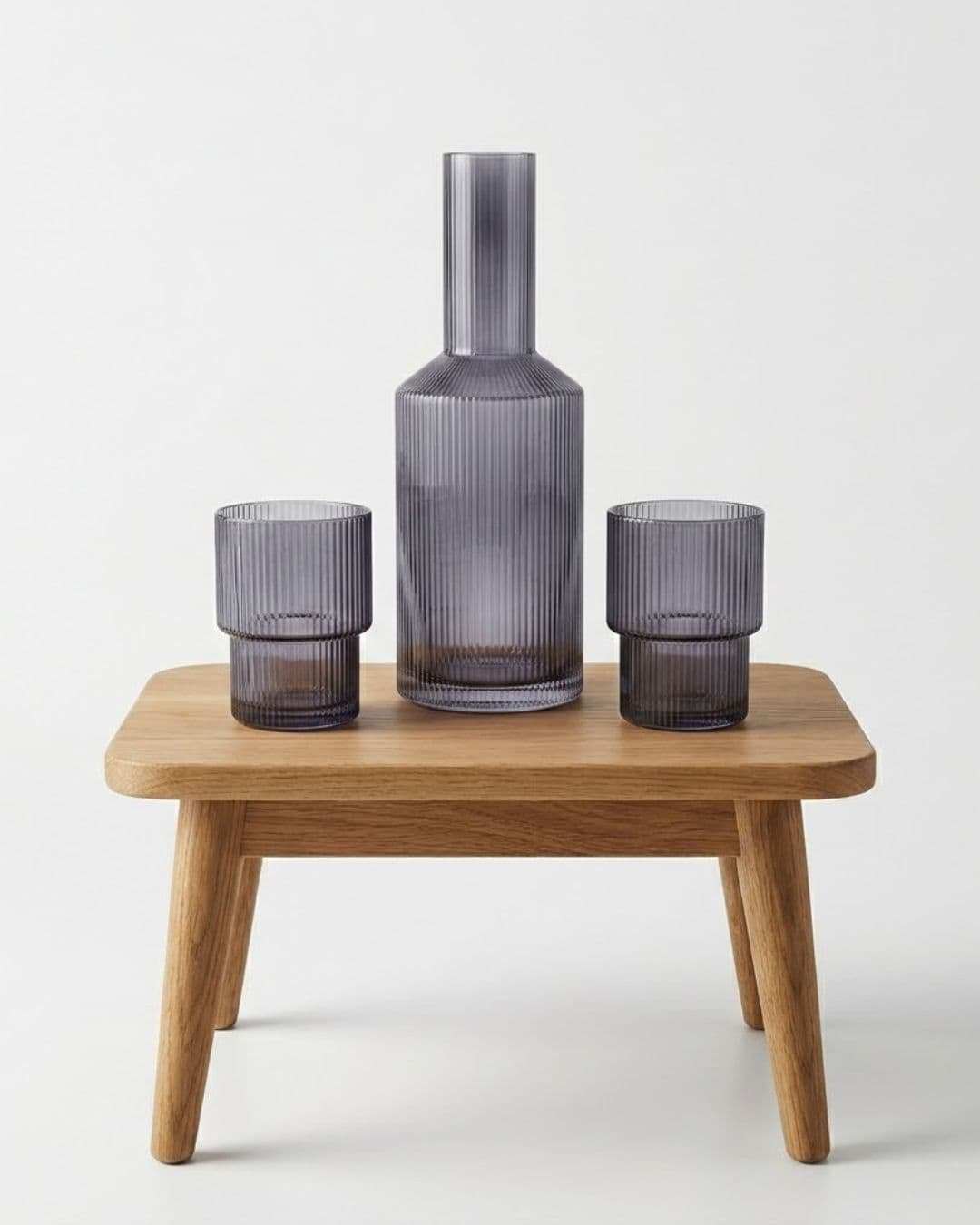 Ribbed glass drinking set with a bottle and two glasses on a wooden stand.
